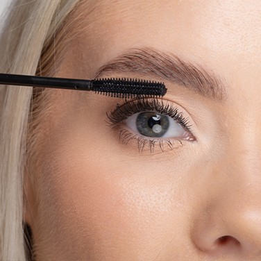 Model glimlacht terwijl ze Nanolash-mascara aanbrengt